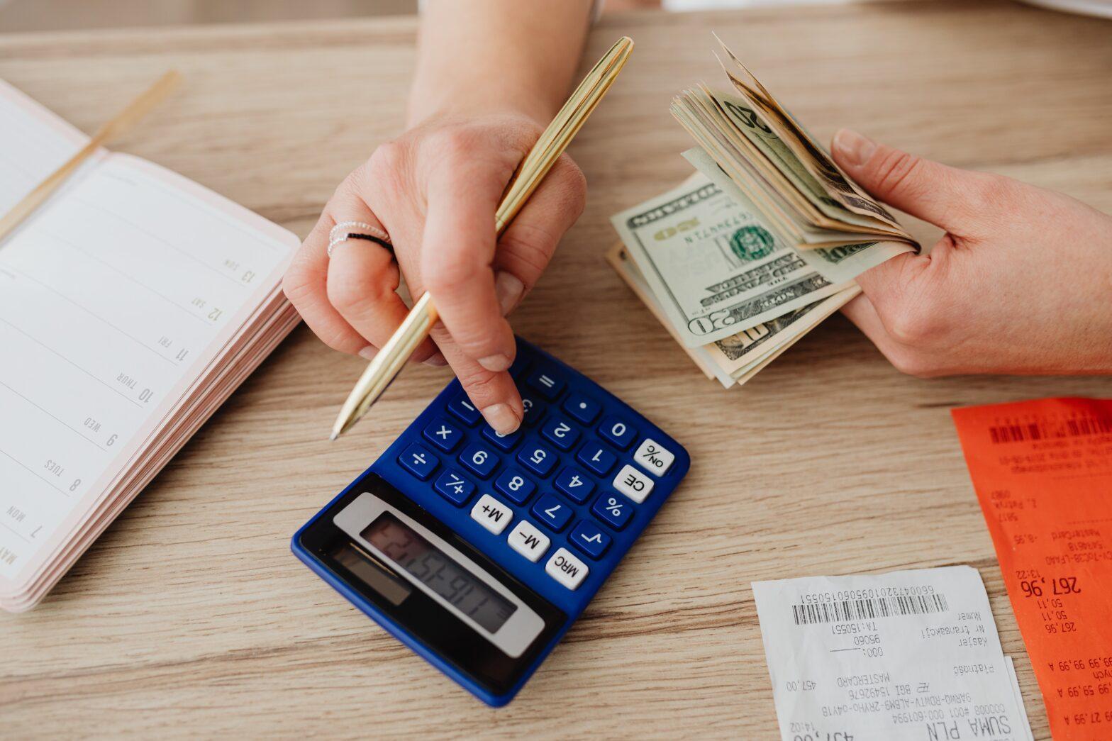 a photo of a person's hand holding a pen and bills and calculating seems to strategize on how to beat inflation by learning to invest